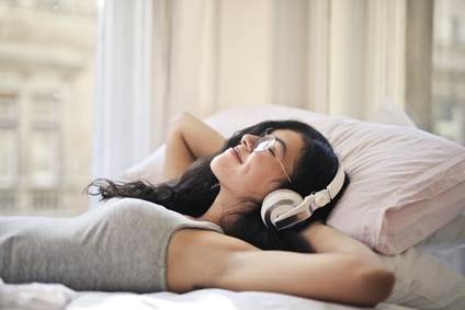 A female with headphones on a bed